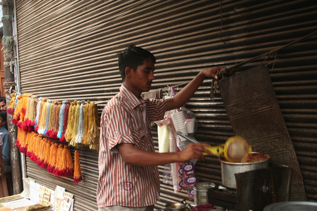 A chai-waala (tea salesman) prepares afternoon tea for all the shop-owners in the area outside a boarded up shop front alongside a stall selling rakhees in the Chandni Chowk market in Delhi.