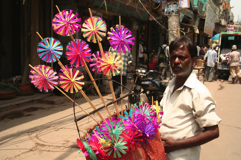 A man selling colorful paper discs adds to the color of the street as he walks around selling his wares in Chandni Chowk market, Delhi.